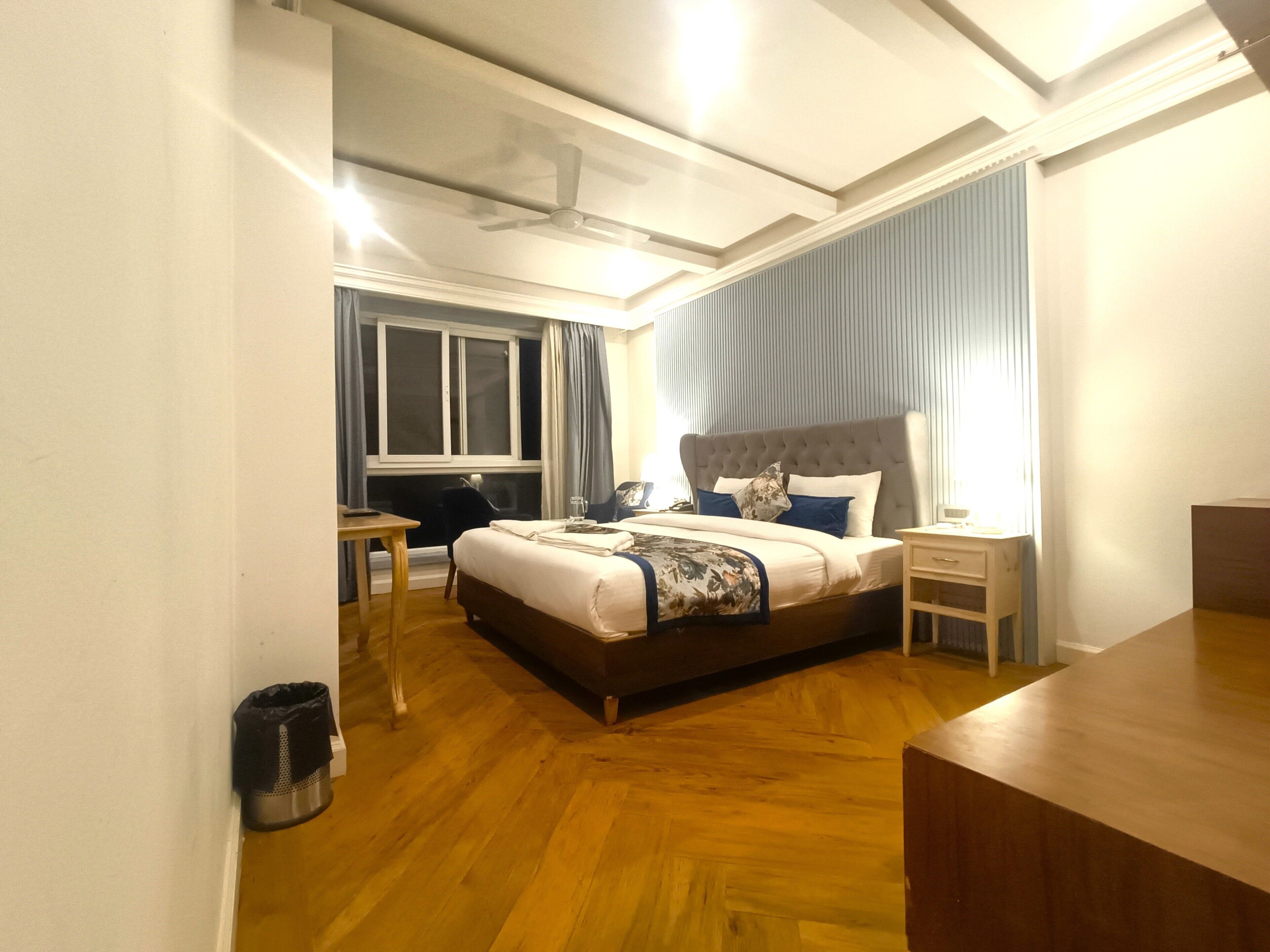 A hotel room with a large bed, a desk, a chair, and a window with curtains.