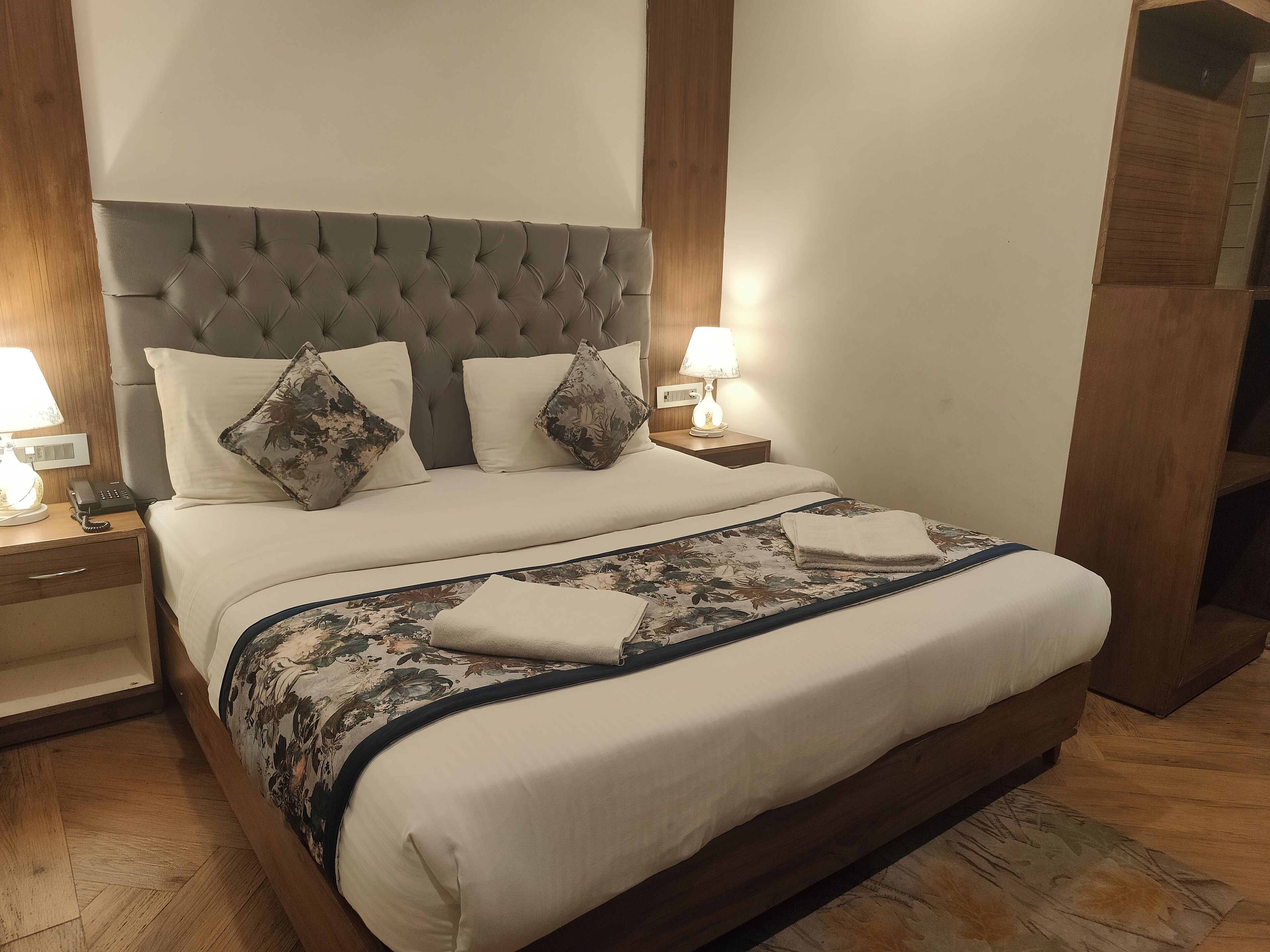 A neatly made bed with a tufted headboard, two bedside lamps, a telephone, and a wooden nightstand.