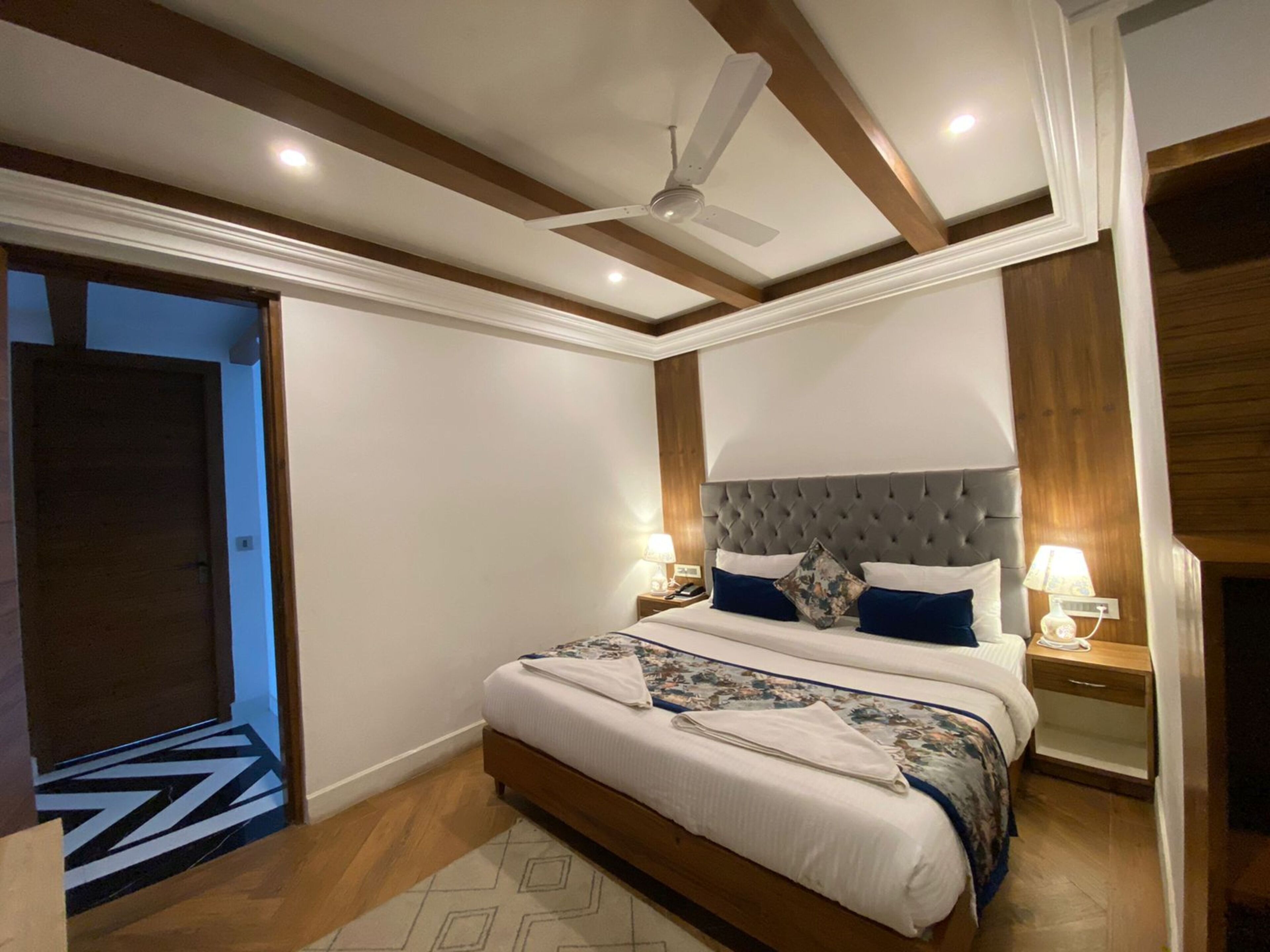A bedroom with a large bed, wooden beams, a ceiling fan, and a nightstand with a lamp.