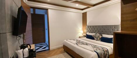A modern hotel room with a large bed, a flat-screen TV mounted on the wall, a ceiling fan, and a wooden headboard.