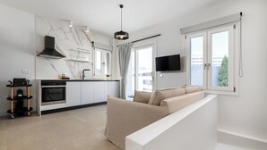 Une cuisine moderne dotée d’un four encastré, d’une hotte noire et d’un coin repas avec une table et des chaises blanches.