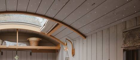 A room with wooden walls, a sloped ceiling with recessed lighting, a skylight, and a wooden beam structure.