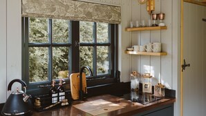 A kitchen with a window, wooden shelves, and a kettle.