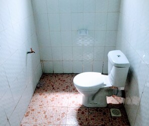 Une petite salle de bain avec des toilettes blanches, des murs carrelés et un sol composé d’un mélange de carreaux blancs et bruns.