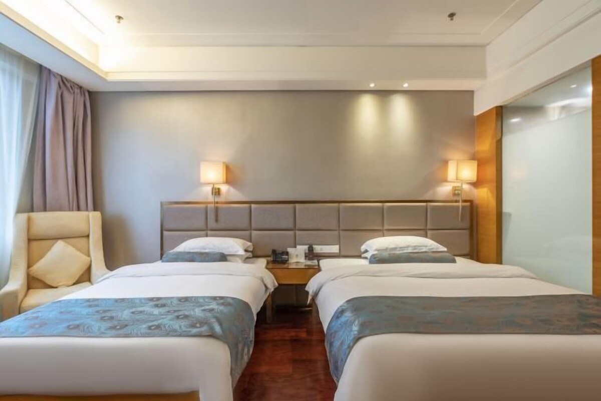 A hotel room with two beds, a chair, a nightstand, and two wall-mounted lamps.