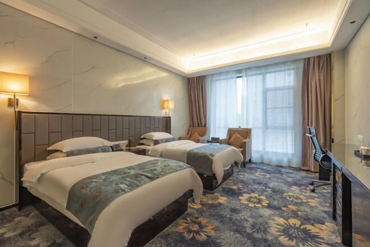 A hotel room with two beds, a desk, a chair, and a TV.