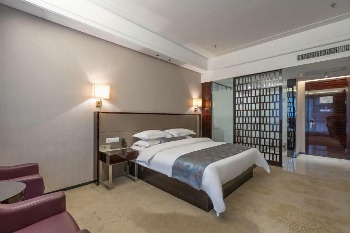 A modern hotel room with a bed, bedside table, lamp, and a seating area.