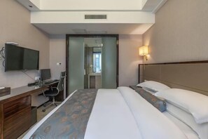 A hotel room with a bed, a desk with a computer, a television, and a wall-mounted lamp. - Fuzhou Linchuan Talent International Hotel (Fuzhou)