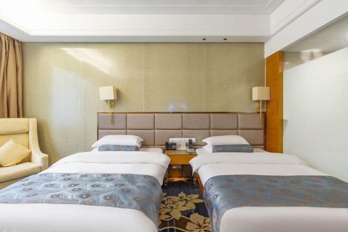 A hotel room with two beds, a sofa, a headboard, lamps, and a telephone.