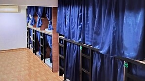A hotel room with a wooden floor, a bed, a desk, and a wardrobe with blue curtains.
