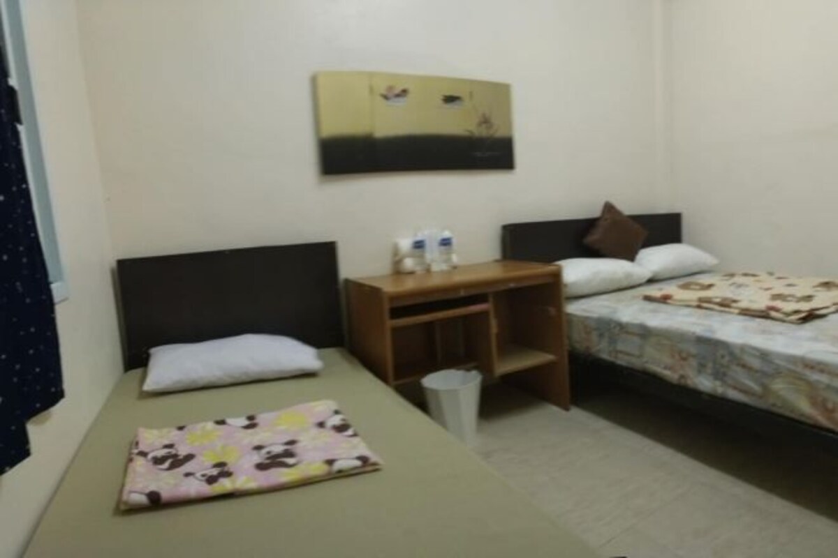 A small, tidy room with two beds, a wooden nightstand, a small table, and a wall-mounted painting.