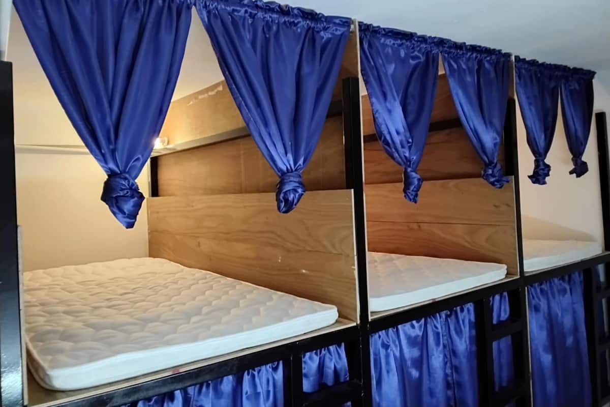 Una cama litera con cortinas azules atadas en la parte superior, cabecero de madera y colchón blanco.