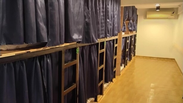A hotel corridor with wooden flooring and a row of dark curtains on the left.