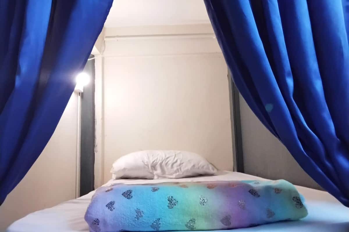 Una cama con un almohadón blanco y una colcha de diseño arcoíris, enmarcada por cortinas azules.