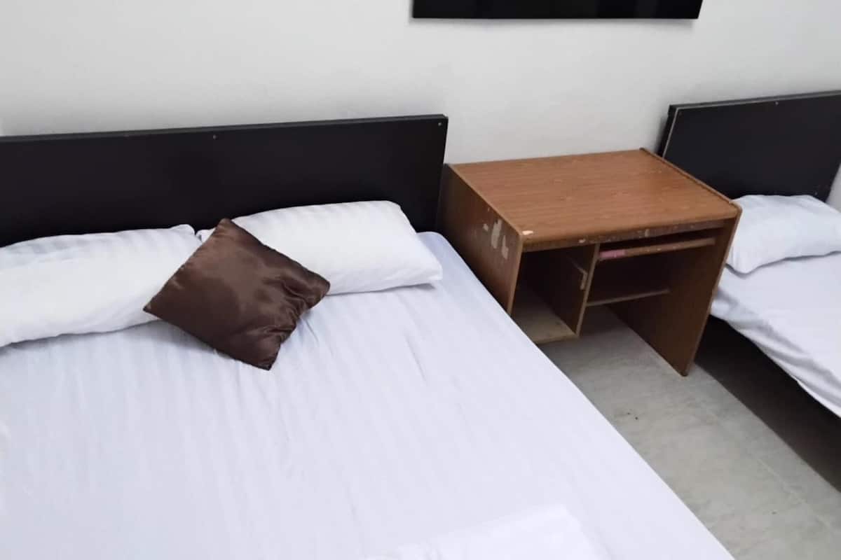 Una cama individual con ropa de cama blanca y un almohadón marrón, una mesita de noche de madera con un estante pequeño y un cabecero negro.