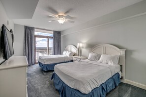 Une chambre d’hôtel avec deux lits, un ventilateur de plafond, un bureau et une grande fenêtre avec des rideaux.