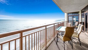 A balcony with a view of the ocean, wicker furniture, and a table.