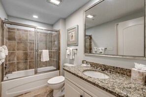 Une salle de bain dotée d’une douche à parois de verre, de toilettes blanches, d’un lavabo surmonté d’un plan de travail en granit et d’un grand miroir.