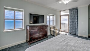 A bedroom with a large bed, a dresser, a television, and a view of the ocean through the windows.