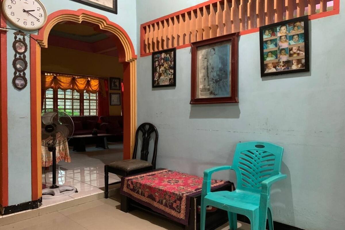 Una habitación con cama, una silla, un reloj y una pared adornada con cuadros.