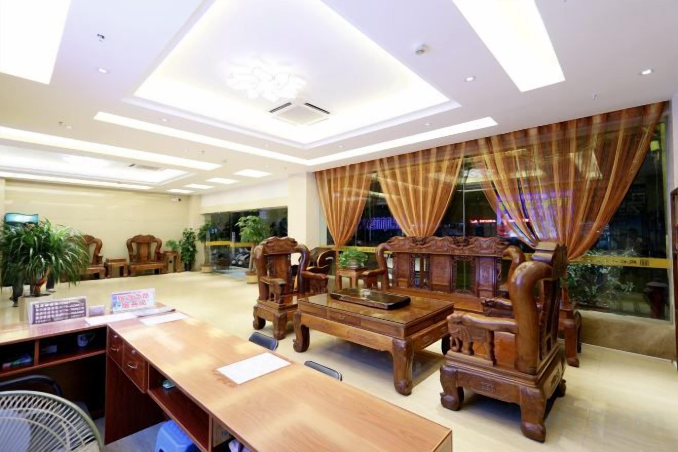 A hotel lobby with a wooden reception desk, comfortable seating, and large windows with curtains.
