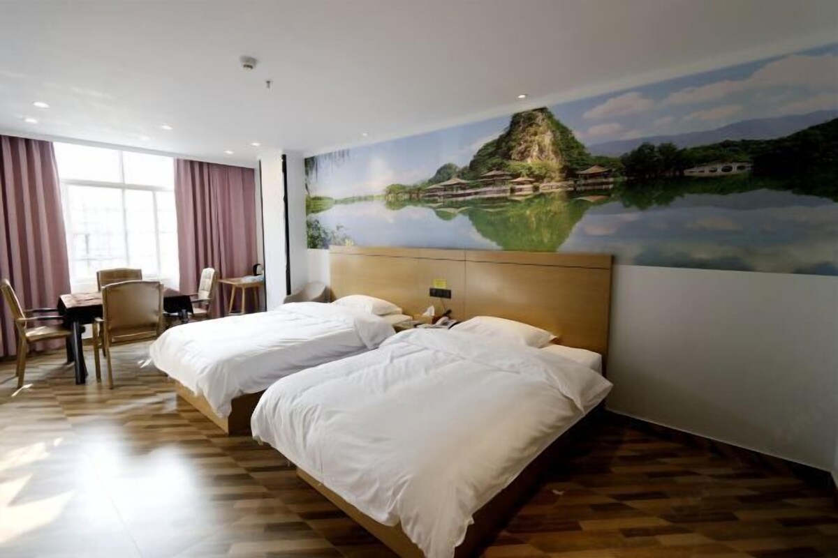A hotel room with two beds, a dining table, chairs, and a large scenic mural on the wall.
