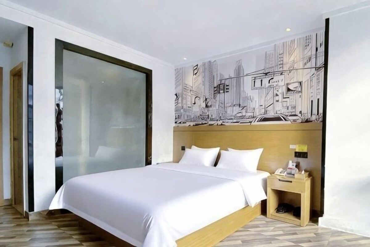 A hotel room with a bed, a nightstand, a wall with a cityscape mural, and a sliding door.