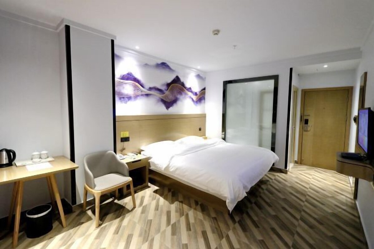 A hotel room with a bed, a desk with a chair, a television, and a wall-mounted artwork.