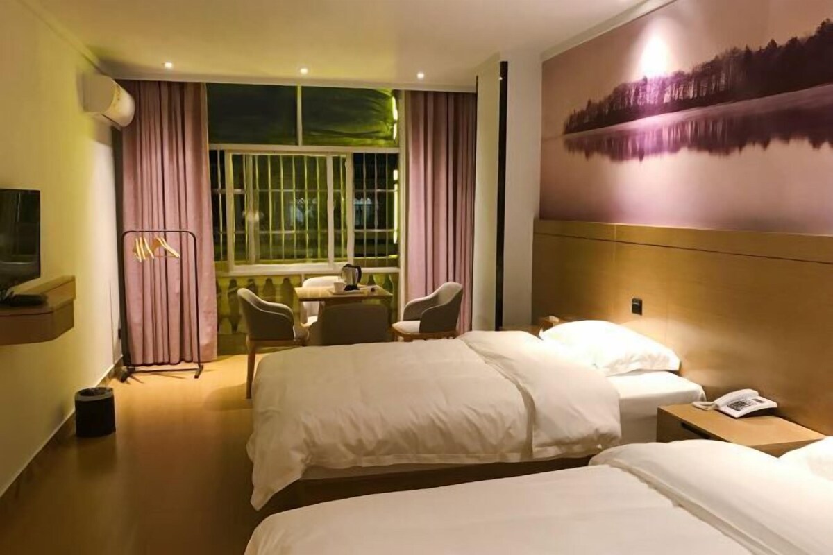 A hotel room with two beds, a desk with chairs, a large window with curtains, and a painting on the wall.