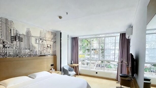 Ein Hotelzimmer mit einem großen Bett, einem Schreibtisch, einem Stuhl, einem Fernseher und einem Fenster mit Blick auf Gebäude.