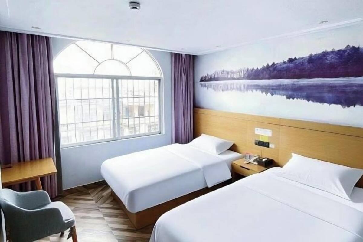 Ein Hotelzimmer mit zwei Betten, einem Schreibtisch, einem Sessel, einem großen Fenster und einem Wandbild.