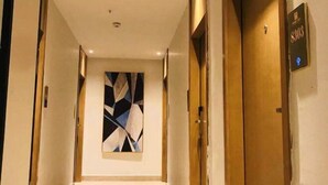 Ein Hotelgang mit einem modernen, abstrakten Gemälde an der Wand, einer Holztür mit einer Zimmernummer und einem hellen Teppich.