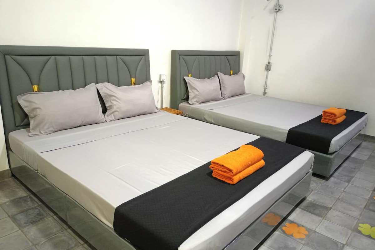 Two single beds with grey headboards and white bedding, a small table with a yellow lamp, and a tiled floor with orange and green flower patterns.
