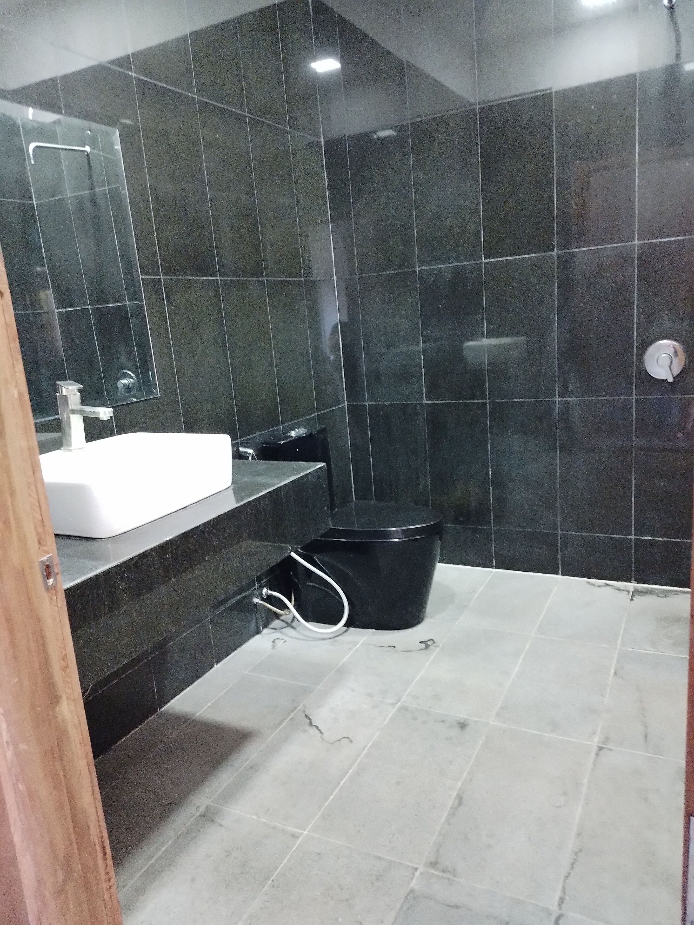 Une salle de bain avec des murs recouverts de carreaux foncés, un lavabo blanc et des toilettes noires.