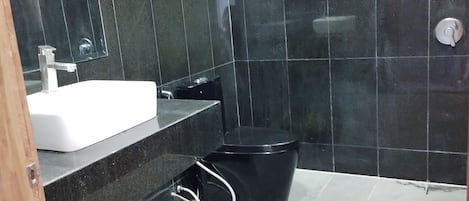 Ein Badezimmer mit dunklen Fliesen, einem weißen Waschbecken und einer schwarzen Toilette.