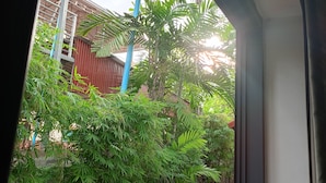 A view through a doorway of a courtyard with dense greenery, including bamboo and palm trees, and a building with a blue roof in the background. - Passport Villa (Siem Reap)