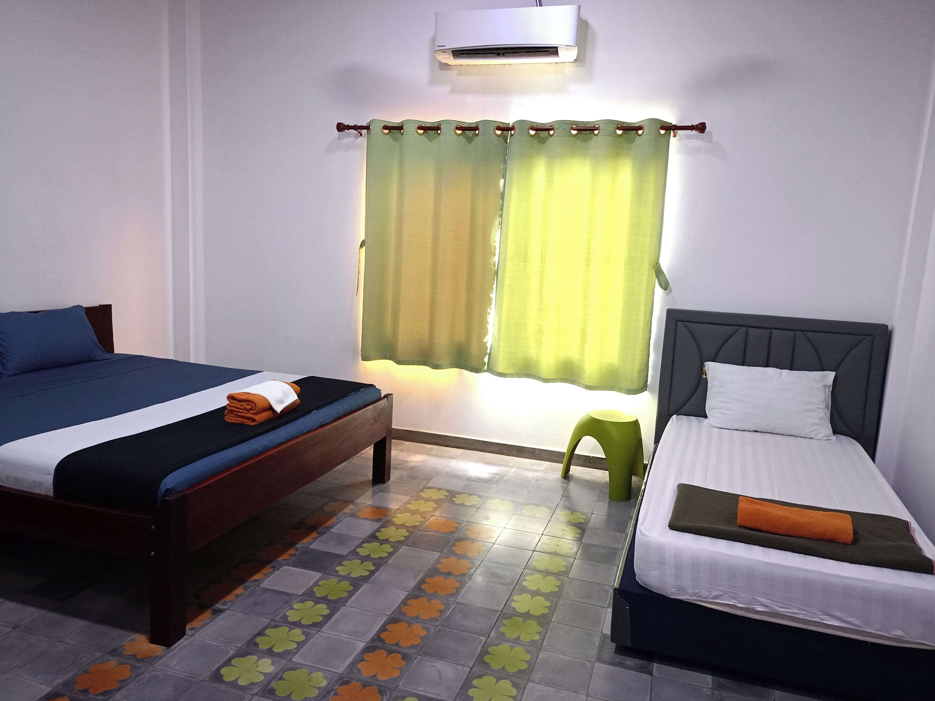 A hotel room with two beds, a window with curtains, an air conditioning unit, and a patterned floor.