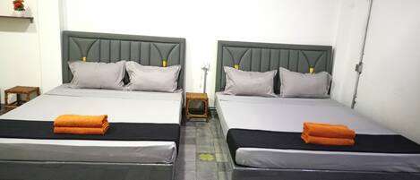 Dos camas individuales con cabeceros grises y ropa de cama blanca, un taburete de madera y un estante de pared con una planta en maceta.