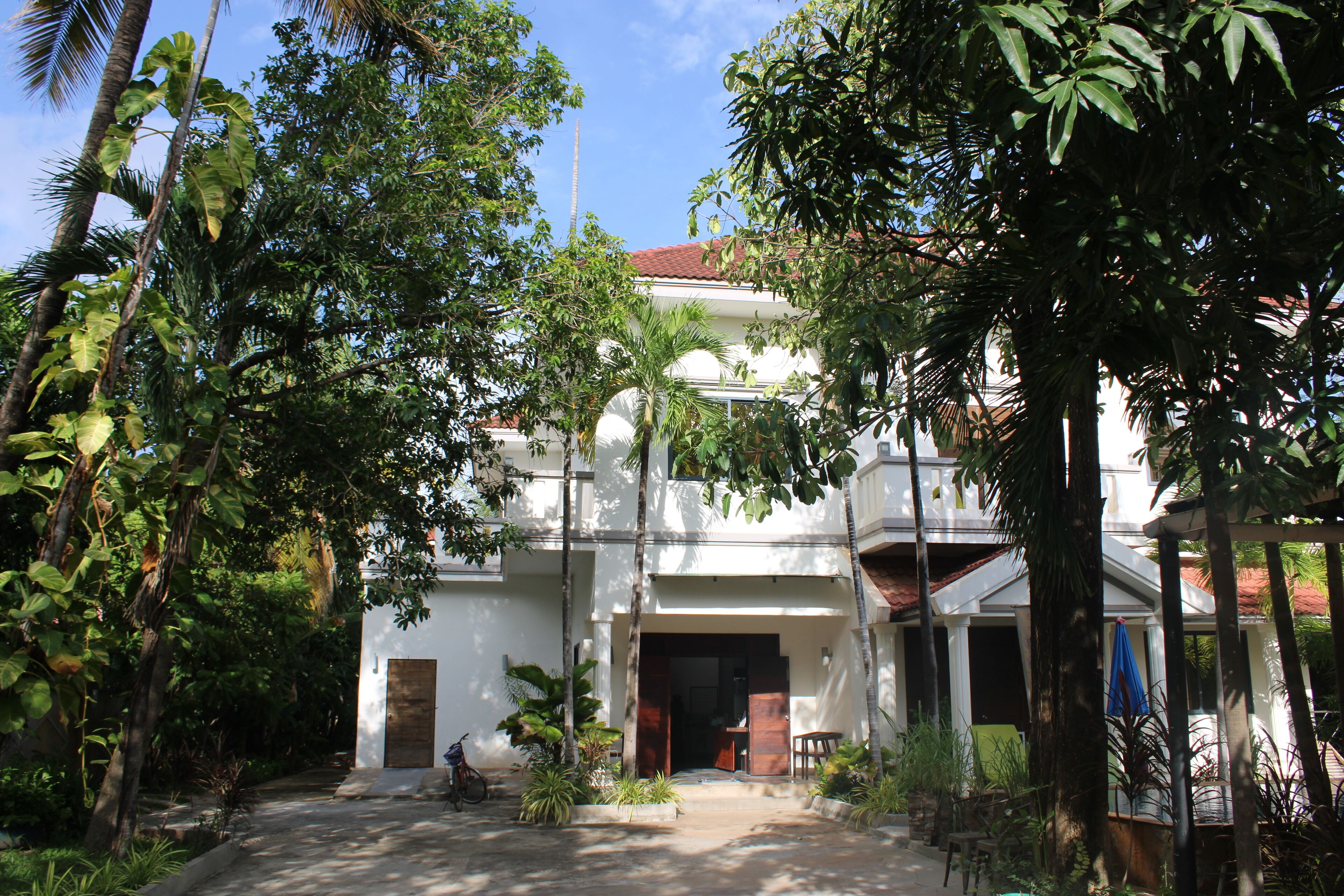 A white building with a red roof, surrounded by lush greenery and palm trees.