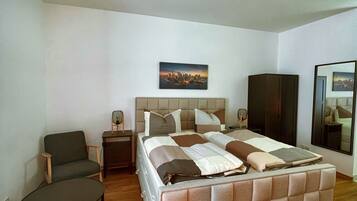 Quarto com uma cama grande, uma cadeira, uma mesa pequena, um espelho e um quadro na parede.