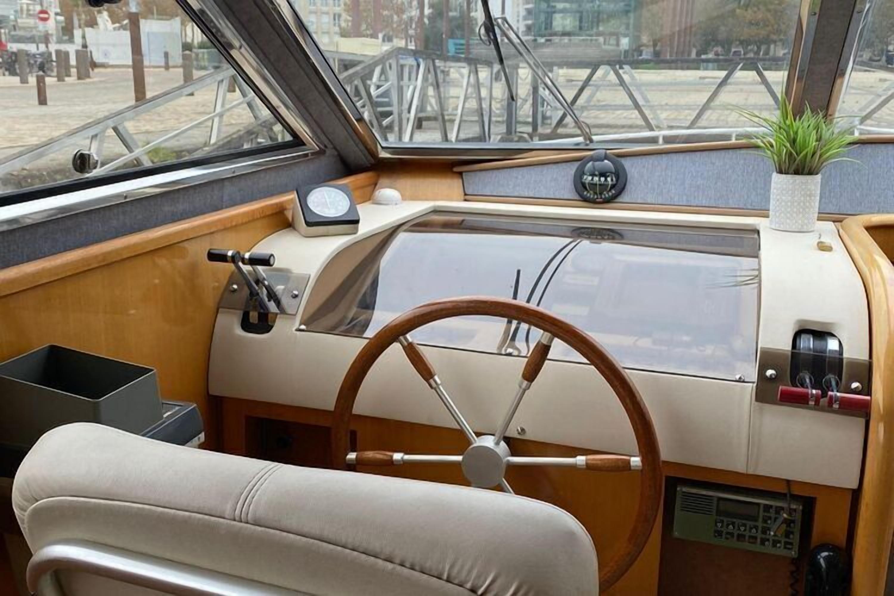 A boat's interior with a steering wheel, wooden paneling, a potted plant, and a control panel.