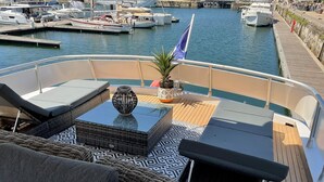 Un pont de bateau agrémenté de meubles en osier, une table avec un vase et un drapeau.