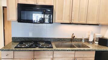 A kitchen with wooden cabinets, a black microwave, a stove, and a sink.