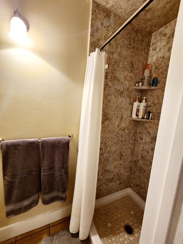 Une salle de bain avec une douche, deux serviettes et une étagère contenant des articles de toilette.