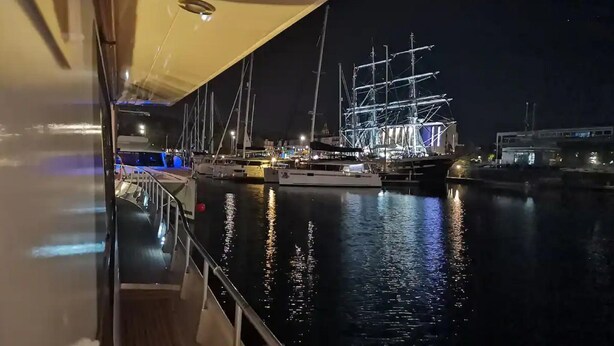 A nighttime marina with boats docked, a covered walkway, and a building with scaffolding in the background. - Luxury yacht in La Rochelle with a terrace (La Rochelle)