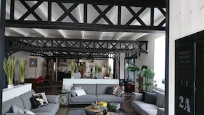 A spacious living area with a high ceiling and exposed beams, furnished with grey sofas and a coffee table.