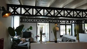 A modern living room with a high ceiling, wooden beams, a sofa, a TV, and potted plants.