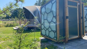A modern, enclosed outdoor structure with a glass facade and wooden frame, surrounded by greenery.