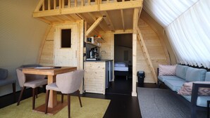 A compact, loft-style room with a wooden staircase, a kitchenette, a sofa, and a dining area.