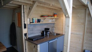 A compact kitchen with a built-in coffee maker, a sink, and a shelf with dishes and glasses.